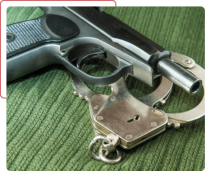 A handgun resting on a pair of metallic handcuffs on a green surface.